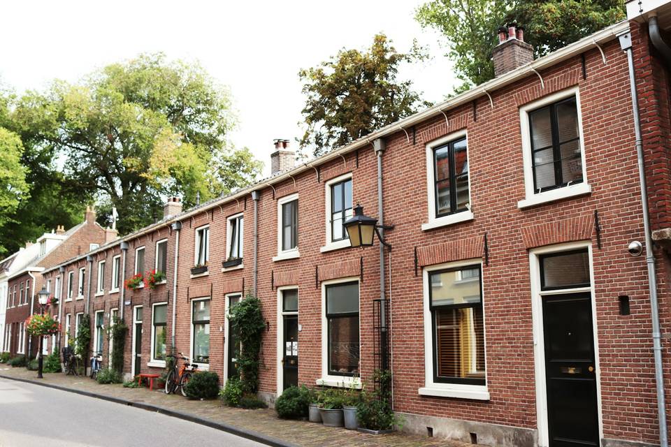 Een rij bakstenen rijtjeshuizen met witte kozijnen in een rustige straat